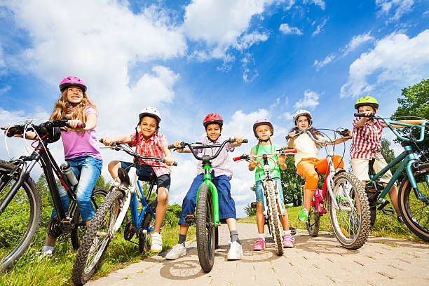 Below angle view of kids in helmets who hold their bikes and stand on path